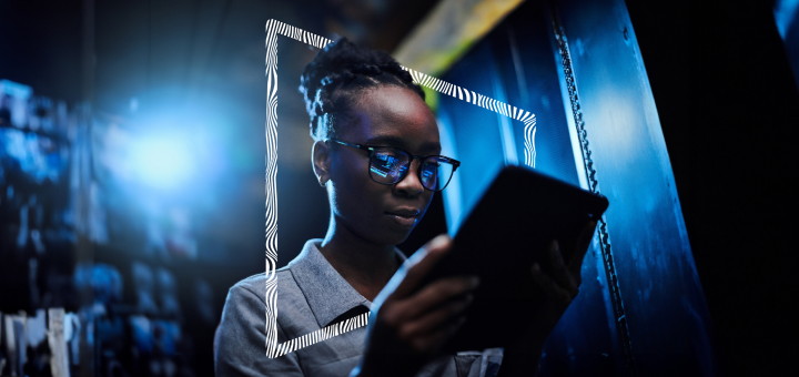 A Black woman looking at a tablet with the screen reflecting in her glasses.